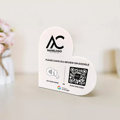 a white sign with a heart shape and a QR code, placed on a table. The sign appears to be a promotional or informational sign, possibly related to a business or service.