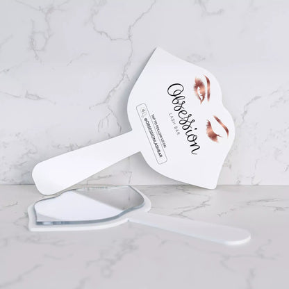 A white makeup brush with a mirror attached to it, placed on a marble surface.