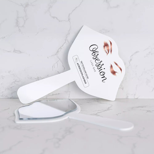 A white makeup brush with a mirror attached to it, placed on a marble surface.