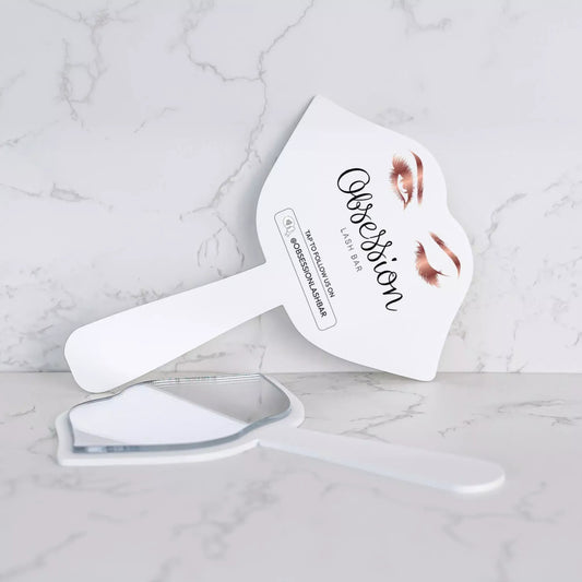 A white makeup brush with a mirror attached to it, placed on a marble surface.